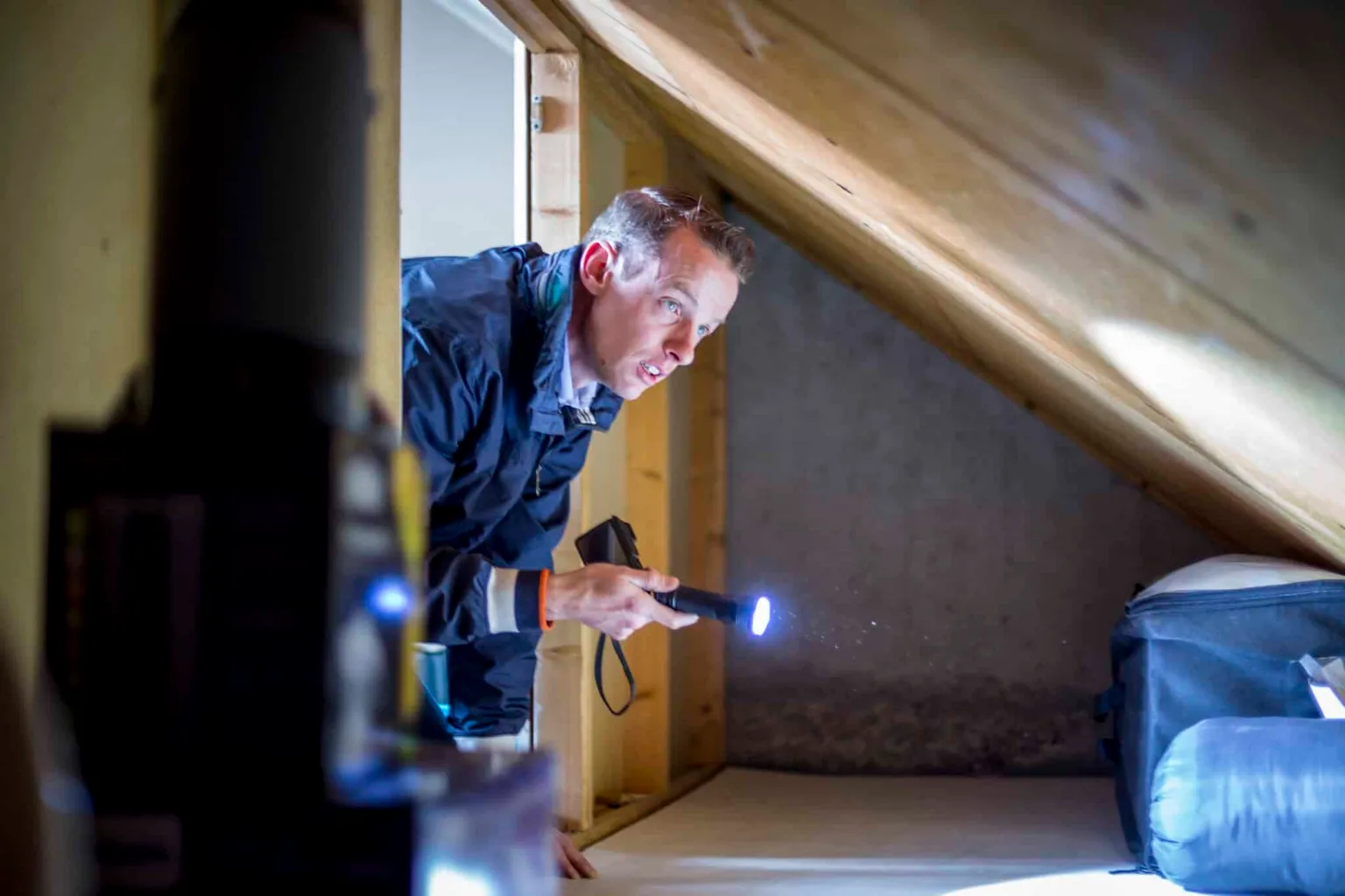 bouwkundig inspecteur bekijkt een scheur in de muur van een oude woonkamer met bouwtekeningen op de vloer